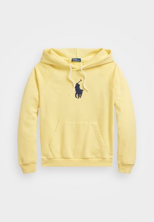 Żółta bluza z kapturem typu pullover z kieszenią z przodu, białymi sznurkami oraz ciemnoniebieskim wyszywanym logo gracza polo na środku klatki piersiowej.