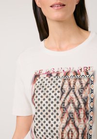 White cotton t-shirt featuring a graphic design with polka dots, geometric patterns, and the text "BE AS YOU ARE," accented with studs.