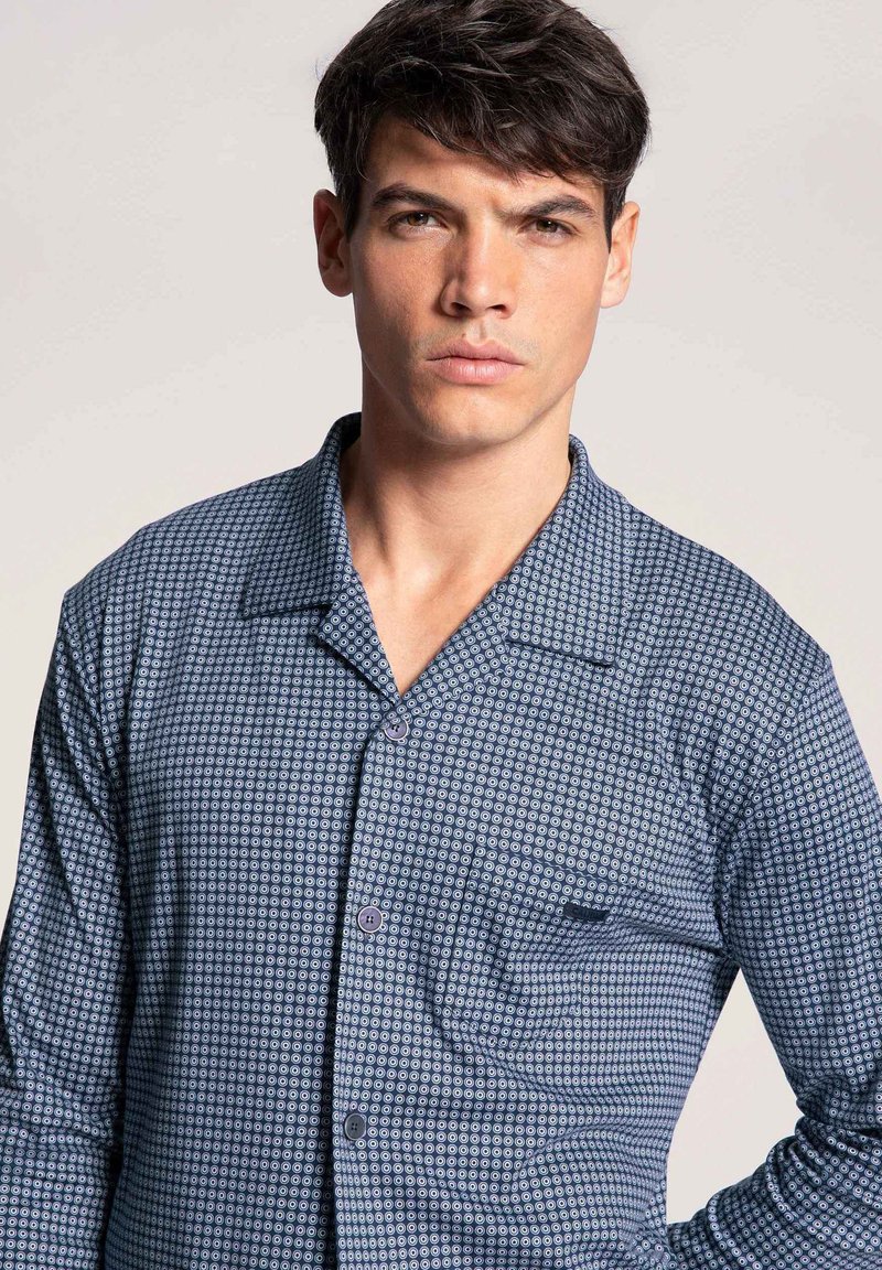 Blauw shirt met patroon, korte revers, voorkant met zak en knopen. Kenmerkt zich door een geometrisch print en een gladde textuur.