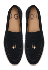 Black suede loafers with a gold accent, featuring a soft upper, contrasting stitching, and a light-colored sole. Smooth texture throughout.
