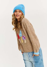 Pletený sveter v hnedej farbe s farebnými aplikáciami húb, doplnený modrou pletenou čiapkou. Textúrovaná tkanina a voľný strih. Svetlomodré manžety.