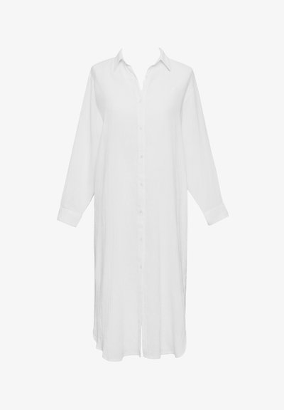 Μακρύ λευκό πουκάμισο από ελαφρύ ύφασμα, με κουμπιά στο μπροστινό μέρος, μυτερό γιακά και μακριά μανίκια με λεπτομέρειες στα μανσέτα.