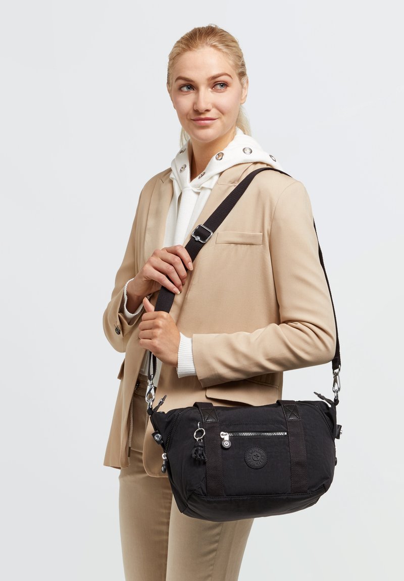 Black fabric shoulder bag with a smooth texture, featuring a silver zipper, a round logo, and adjustable strap. Compact and versatile design.