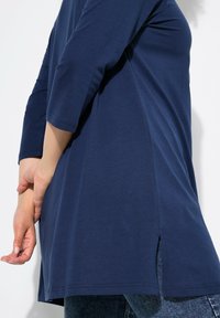 Navyblauer Tunika-Top mit 3/4-Ärmeln aus weichem Stoff, mit seitlichen Schlitzen am Saum für Bewegungsfreiheit und Komfort.