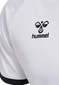 T-shirt de sport blanche avec un logo noir au design abstrait sur la poitrine, fabriquée en tissu lisse et respirant, rehaussée d'une bordure noire.