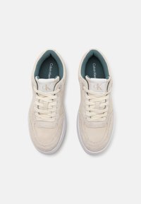 Sneakers Calvin Klein in suede beige con suole in gomma bianca. Presentano un design con lacci e un tessuto morbido e testurizzato. Interno foderato in teal.