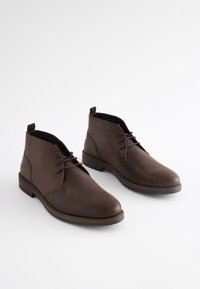 Hnedé kožené členkové čižmy s hladkou textúrou, okrúhlou špičkou a šnúrkami. Dizajn má jednoduchý tvar a jemný šijací detail.