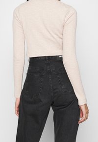 Haut cropped rose clair à manches longues côtelées, associé à un pantalon en denim noir taille haute avec poches arrière et ceinture à logo.