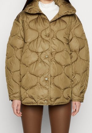 Brun quiltet jakke med uregelmæssig afrundet syning, trykknapper foran, båret over en hvid top og kombineret med brune leggings.