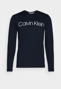 Czarna koszulka z długim rękawem wykonana z bawełny, z białym logo "Calvin Klein" na wysokości klatki piersiowej, z okrągłym dekoltem i dopasowanymi rękawami.