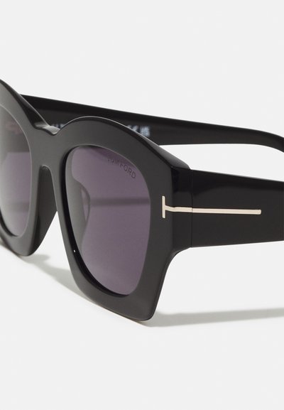 Occhiali da sole neri con montatura oversize e angolare. Lenti oscurate presentano un accento dorato sul lato, con "TOM FORD" impresso sulla stecca.