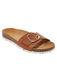Sandalia de cuero marrón con una gran hebilla circular dorada, plantilla de corcho y suela blanca salpicada. Diseño plano y estilo de punta abierta.