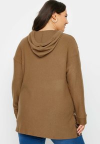 Brązowy, prążkowany hoodie z kangurzą kieszenią i kapturem. Z boku znajdują się rozcięcia z akcentem w panterkę. Długie rękawy, luźny krój.