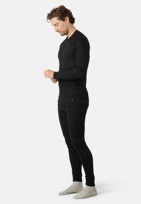 Sort termisk top og leggings, ribbet tekstur, tætsiddende design, lange ærmer, rund halsudskæring, parret med lysegrå sokker.