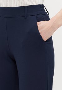 Navy blue pants with a smooth, stretchy material. Features an elastic waistband and side pocket, with a fitted design and clean lines.