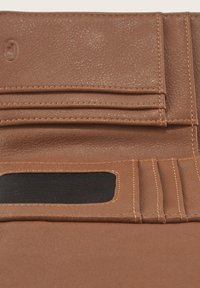Portafoglio in pelle marrone con superficie testurizzata, multiple fessure per carte e una sezione in tessuto nero. Presenta cuciture visibili e bordi lisci.