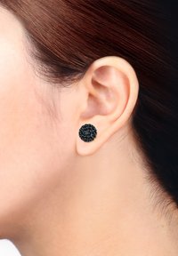Runde schwarze Steckerohrringe mit einer strukturierten Oberfläche, versehen mit einem Cluster aus kleinen, glänzenden schwarzen Steinen. In einer schlichten Metallbasis gefasst.
