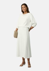 Ensemble blanc en deux pièces comprenant un haut ample à manches longues et une longue jupe. Tissu lisse avec une coupe décontractée et des détails de drapés subtils.
