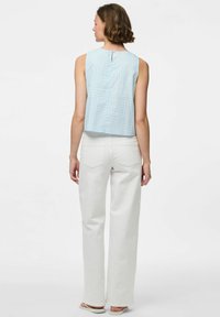 Svijetloplava majica bez rukava s kariranim uzorkom, s otvorom na leđima, u kombinaciji s bijelim širokim hlačama. Glatka tekstura tkanine.