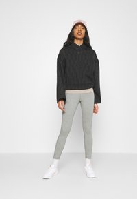 Zwart geruite cropped hoodie met wijde mouwen, gedragen over een beige top, gecombineerd met grijze leggings en witte sneakers; zachte stof.