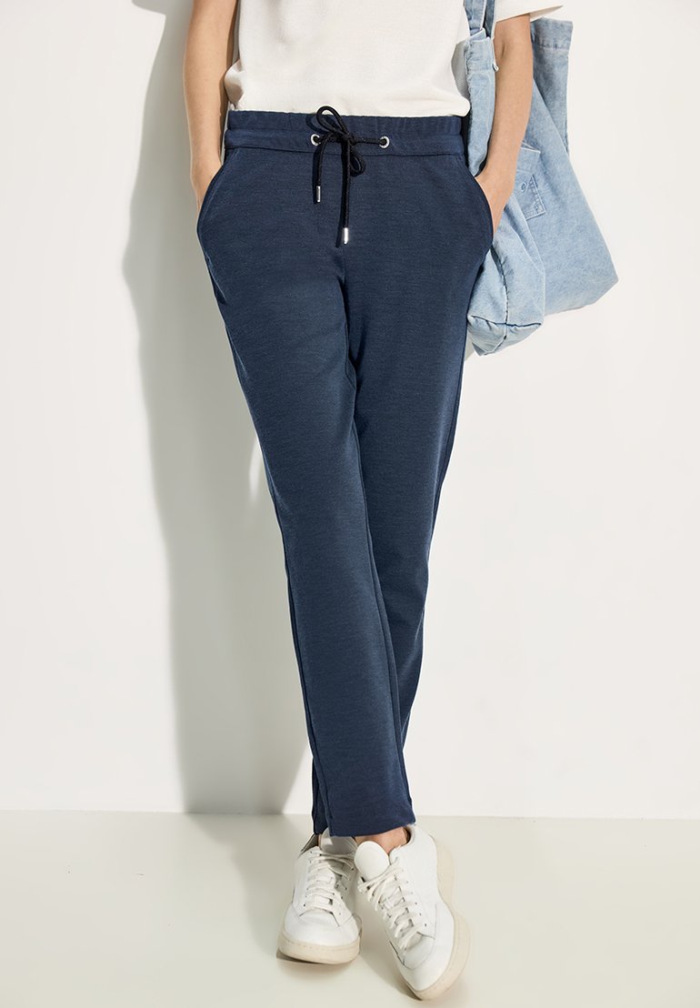 Marineblauwe joggerbroeken met een elastische tailleband, zijzakken en taps toelopende benen, gecombineerd met witte sneakers en een lichtblauwe totebag.