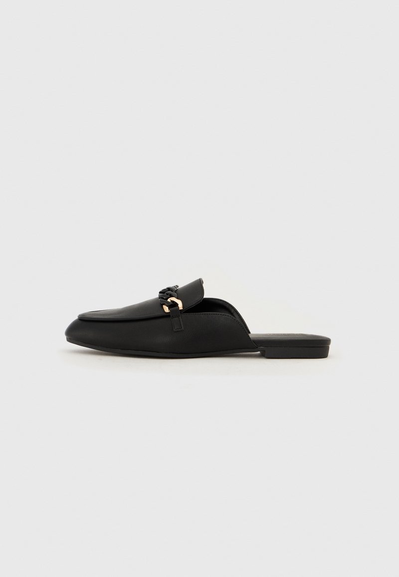 Mule en cuir noir sans bride avec un petit talon et un détail décoratif en chaîne dorée et noire sur le dessus, présentée de profil sur un fond uni.