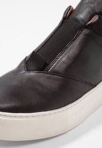 Svarta lädersneakers med elastiskt panel, sömdetaljer och en texturerad vit gummisula. Vinklad tå och minimalistisk design.