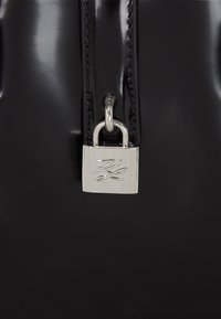 Sac à main noir en cuir verni avec une finition brillante, doté d'un fermoir à cadenas en argent et de surpiqûres décoratives le long des poignées.