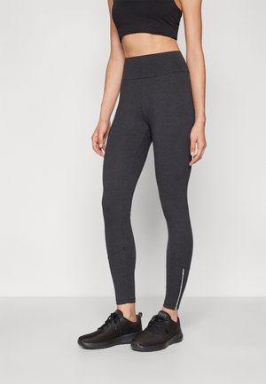 Leggings de sport noirs avec une taille haute, une coupe cintrée et des accents zippés aux chevilles, associés à des baskets noires à texture.
