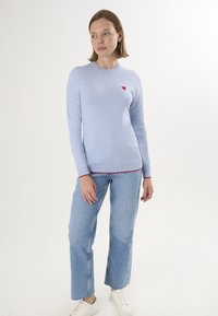 Maglione azzurro chiaro a maniche lunghe con scollo rotondo, caratterizzato da un piccolo cuore rosso sul petto e bordi rossi a contrasto sull'orlo.