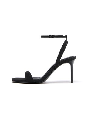 Črna sandala z visokimi petami, tankim trakom okrog gležnja, kvadratnim prstom in salonarsko peto na belem ozadju.