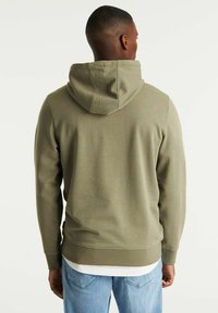 Olive green hoodie with a hood, ribbed cuffs, and waistband. The fabric appears soft with a smooth texture, worn over a white shirt.