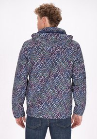 Jachetă cu glugă pe un fundal albastru închis, având un model geometric colorat. Fabricată dintr-un material ușor, are mâneci lungi și o croială lejeră.