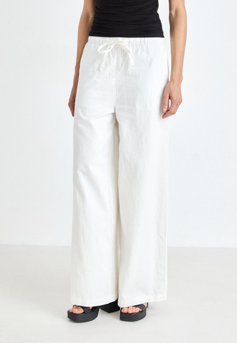 Wide-leg, white pants with a textured fabric and elastic waistband, featuring a drawstring. The outfit is paired with black platform sandals.