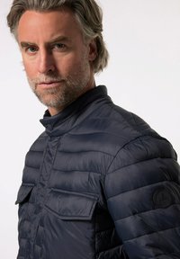 Marineblaue Daunenjacke mit horizontalem Steppmuster, hohem Kragen und zwei Brusttaschen. Verfügt über ein rundes Logopatch am linken Ärmel.