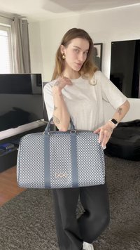 Sac à main bleu à motif avec des anses bleu foncé, forme rectangulaire, détail de logo doré, et surface en tissu texturé.