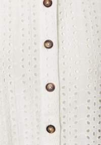 Weißes Hemd mit Knopfverschluss, das mit einem gestickten Lochmuster, sechs braunen Knöpfen und einem weichen, strukturierten Stoff versehen ist.