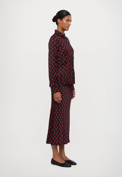 Set din rochie și fustă neagră cu model de semicerc roșu. Mâneci lungi, guler, материал ușor, și pantofi negri fără toc. Vedere din profil lateral.