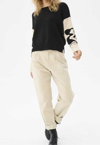 Pull en tricot noir avec manches beige à motifs, associé à un pantalon ample beige et des bottines noires.