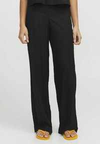 Zwarte losse broek van lichtgewicht stof, met een gladde textuur en een vloeiende silhouet. Draag slippers in het geel.