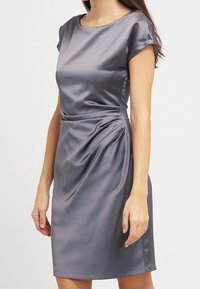 Robe en satin gris avec manches courtes, encolure ronde et drapé latéral. Texture lisse et silhouette cintrée, longueur au genou.