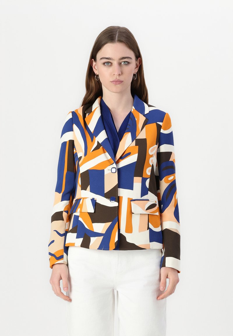 Blazer colorato a fantasia in arancione, blu e crema, con revers appuntiti, due tasche frontali e una vestibilità aderente. Abbinato a una blouse blu.