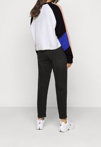 Sweatshirt en color-block, avec un corps blanc, des manches noires, et des accents en rose clair et bleu ; porté avec un pantalon sombre et des baskets blanches.