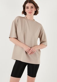 Beige oversized t-shirt med korte ærmer, rund halsudskæring, glat tekstur, parret med sorte cykelshorts. Enkel og nutidig design.
