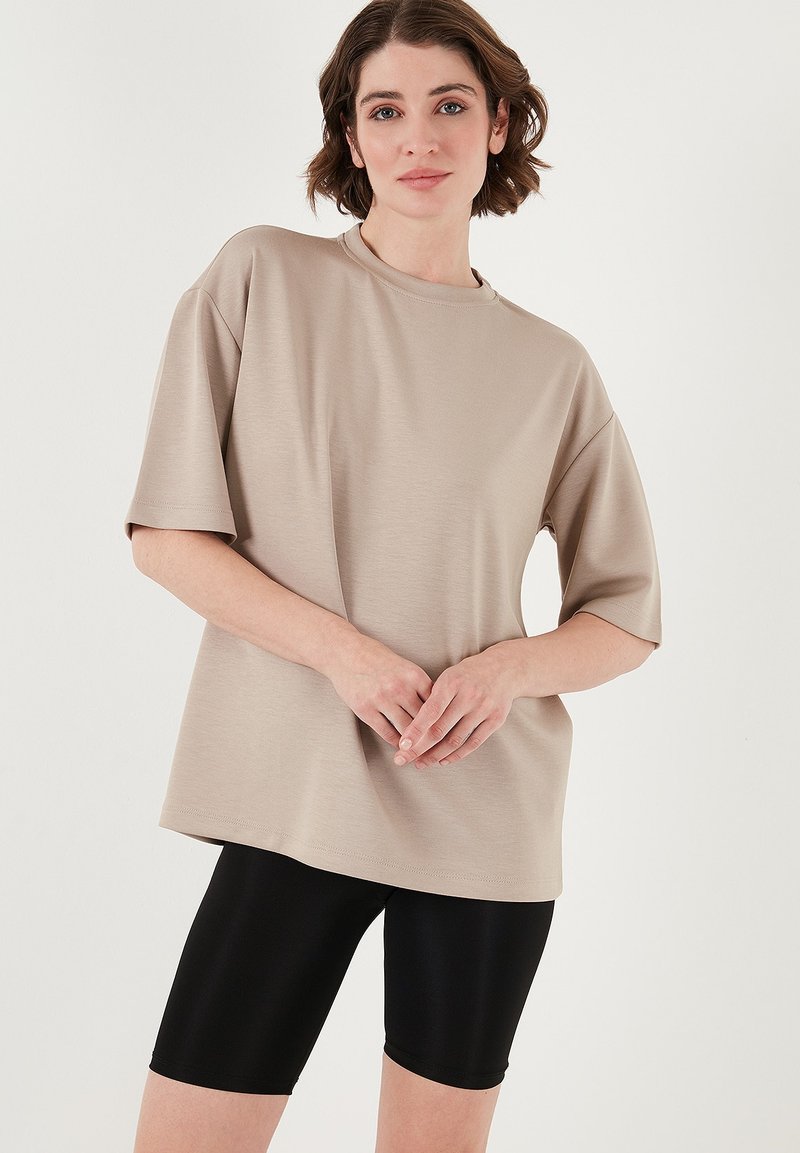 Beige oversized t-shirt med korte ærmer, rund halsudskæring, glat tekstur, parret med sorte cykelshorts. Enkel og nutidig design.