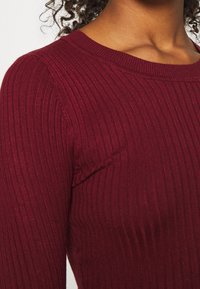 Top a costine bordeaux con scollatura rotonda. Il tessuto presenta un motivo testurizzato con linee orizzontali e un design aderente.