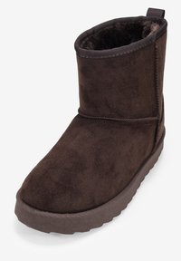 Stivale alla caviglia in suede marrone con una morbida fodera interna, punta arrotondata e bordo superiore rigato. Presenta una suola in gomma texturizzata per la trazione.