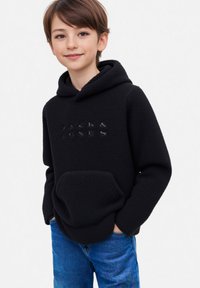 Czarna polarowa bluza z kapturem z kangurzą kieszenią i wytłoczonym logo z przodu, w połączeniu z niebieskimi dżinsami. Miękka tekstura i swobodny krój.