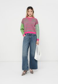 Pulover tricotat cu un model în dungi roz și verde, purtat cu blugi evazați albaștri cu talie înaltă și o geantă albă. Texturi fine în întreaga ținută.