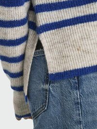 Gestreepte gebreide trui in blauw en crème, met ribgebreide manchetten en een zijsplit. Gecombineerd met vervaagde blauwe denim jeans.